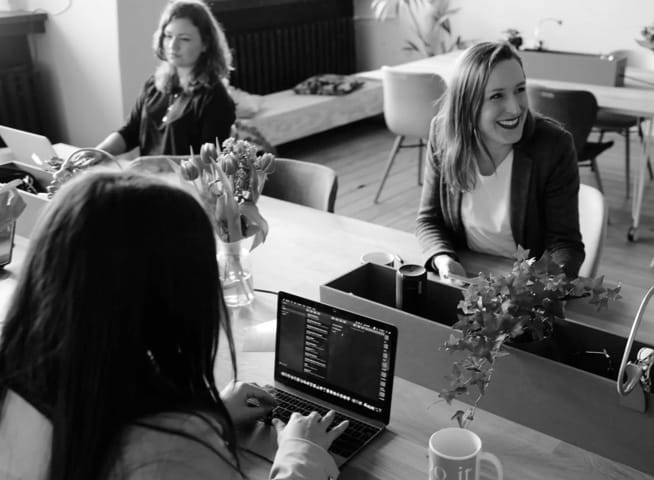 people working on laptops around a table, talking and laughing